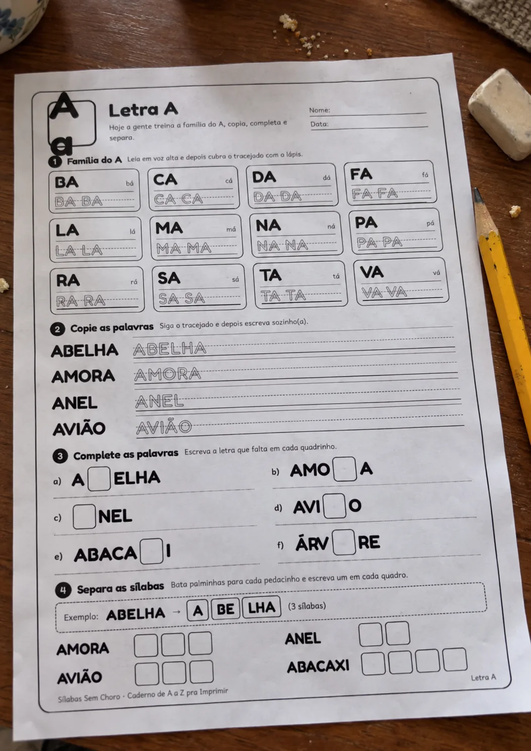 Folha da letra A do caderno impressa sobre uma mesa de madeira, com lápis e borracha ao lado